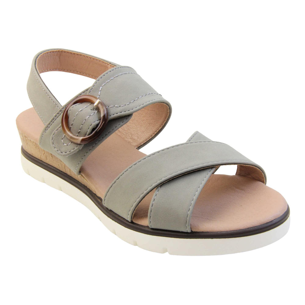 Memory foam wedge sandals. Classic womens strappy sandals with grey textile straps. Dual toe straps that cross over each other. The ankle strap is touch fasten but has a brown buckle detail to look like a buckle fastening. Beige faux leather memory foam insoles. Small wedge heel in cork effect. White outsole with a black rim around the top. Right foot at an angle.
