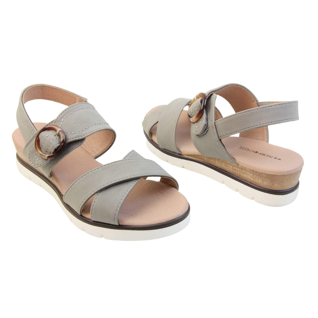 Memory foam wedge sandals. Classic womens strappy sandals with grey textile straps. Dual toe straps that cross over each other. The ankle strap is touch fasten but has a brown buckle detail to look like a buckle fastening. Beige faux leather memory foam insoles. Small wedge heel in cork effect. White outsole with a black rim around the top. Both shoes about an inch apart at a slight angle facing top to tail.