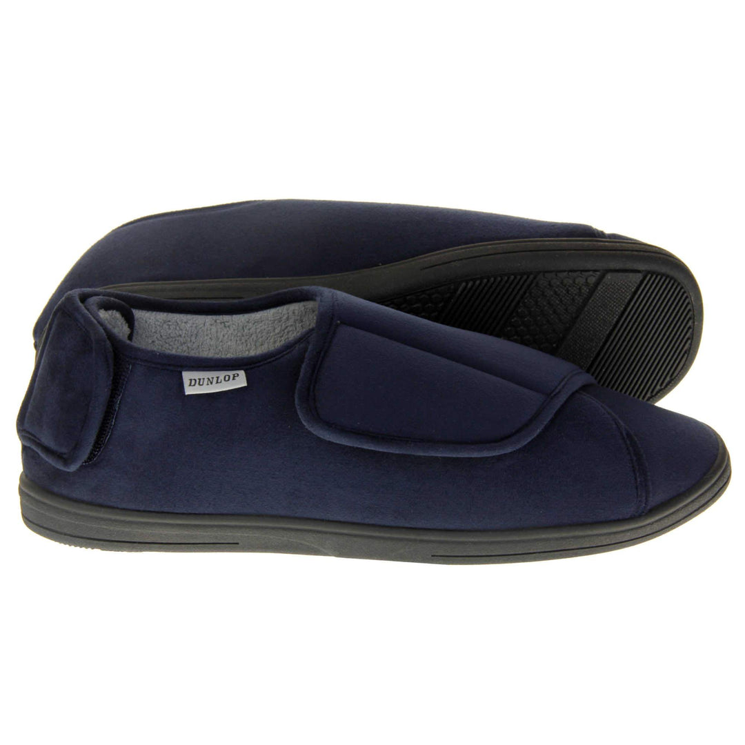 Mens adjustable slippers. Full back slippers with navy blue upper. Adjustable touch fasten strap to the top of the foot and around the back of the heel. Small white label on the outside rim, with Dunlop branding sewn in black. Grey faux fur lining. Both feet from side profile with left foot on its side to show the sole.
