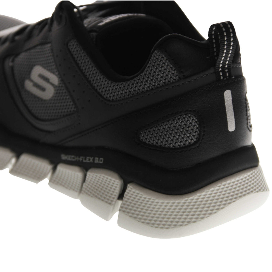 Mens black Skechers. Dark grey mesh and black leather upper with black laces and black lining. Grey Skechers logo to the side and chunky white outsole with grip. Close up of the back of the shoe to show the Skechers detail.