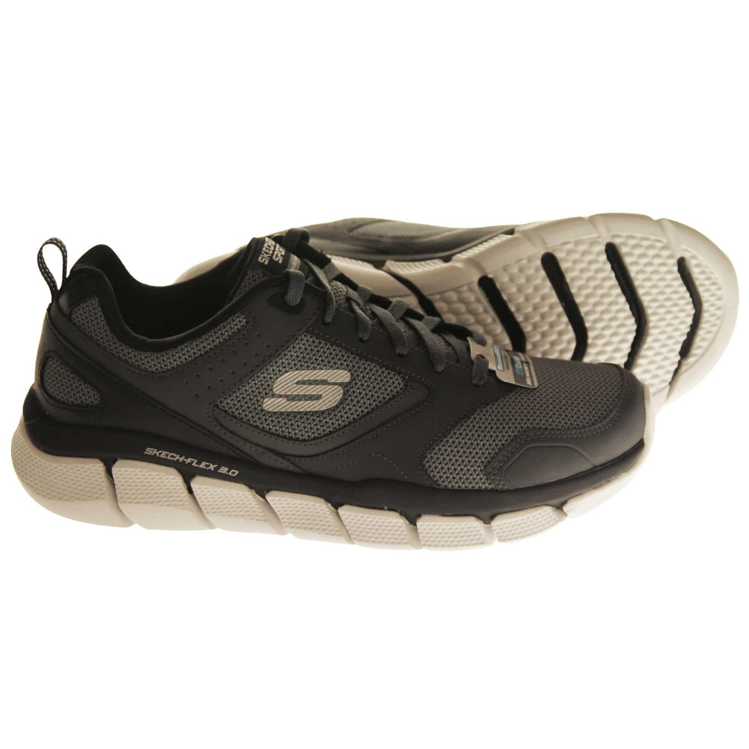 Mens black Skechers. Dark grey mesh and black leather upper with black laces and black lining. Grey Skechers logo to the side and chunky white outsole with grip. Both feet from a side profile with the left foot on its side to show the sole.