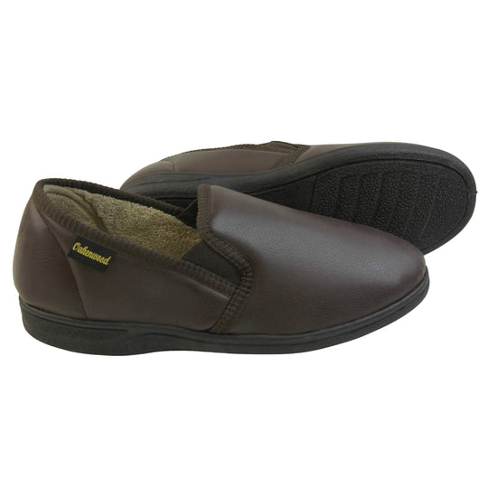 Mens faux leather slippers. Brown faux leather classic full back slipper with beige fleece lining. Both feet from side profile with left foot on its side to show the sole.
