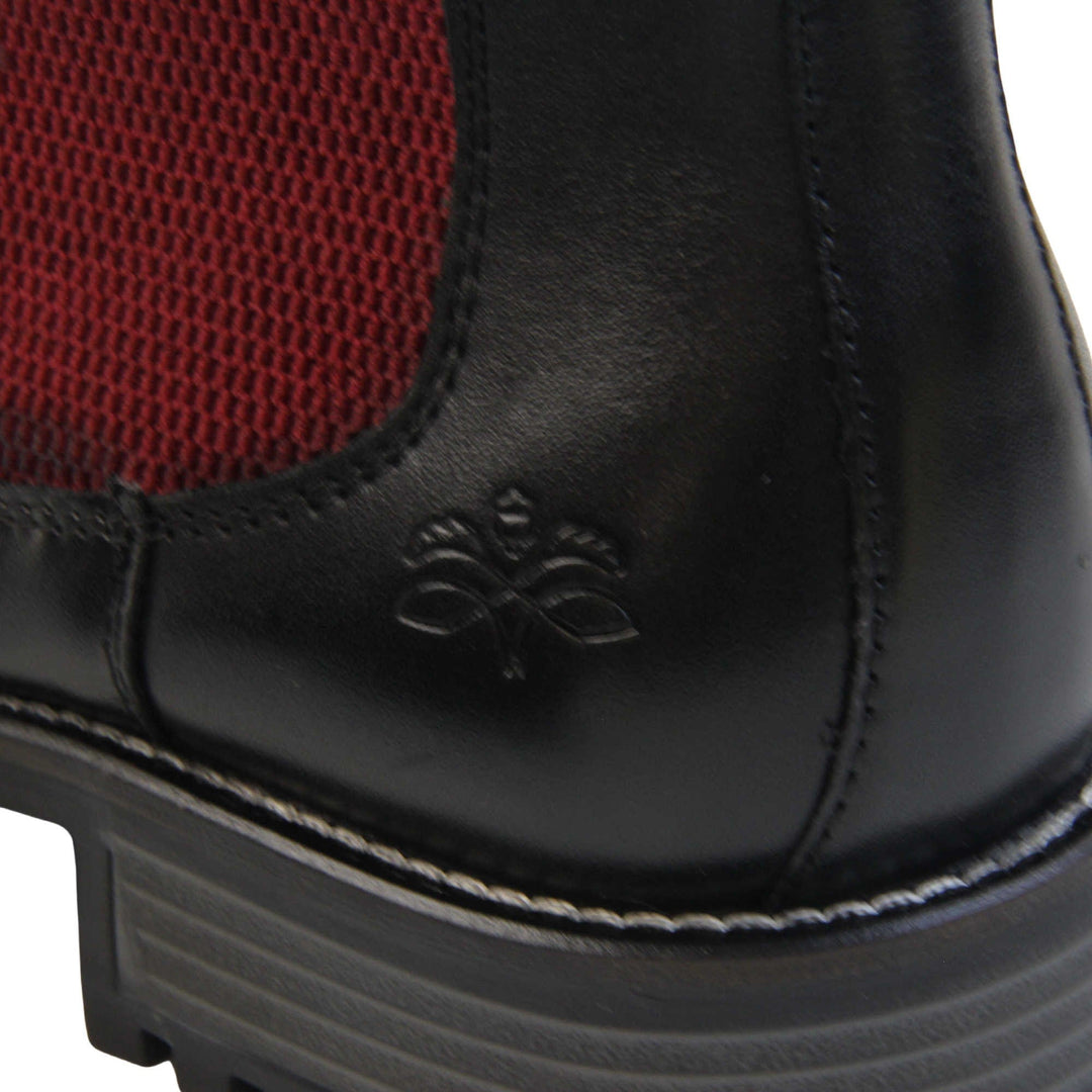 Mens leather Chelsea boots black. Ankle boots with black leather uppers and red textile elasticated side panels. Red textile tab to the back rim to help pull shoes on. Embossed Oakenwood brand to the outside heel of the boot. Black sole with very slight heel. Left foot close up of the heel of the shoe to show the embossed branding on the heel of the shoe.
