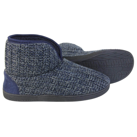 Mens memory foam slippers. Slipper boots with a navy blue knit upper. Navy fabric piping around the collar. Navy textile patch over the heel to reinforce. Thick black synthetic sole with Dunlop branding on. Navy faux fur lining. Both slippers from side profile with left foot on its side behind the right to show the sole.