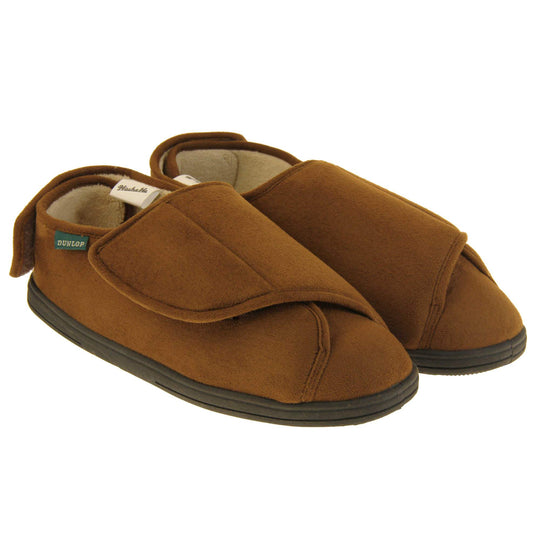 Mens adjustable slippers. Full back slippers with brown upper. Adjustable touch fasten strap to the top of the foot and around the back of the heel. Small white label on the outside rim, with Dunlop branding sewn in black. Cream faux fur lining. Firm black sole. Both feet together at an angle.