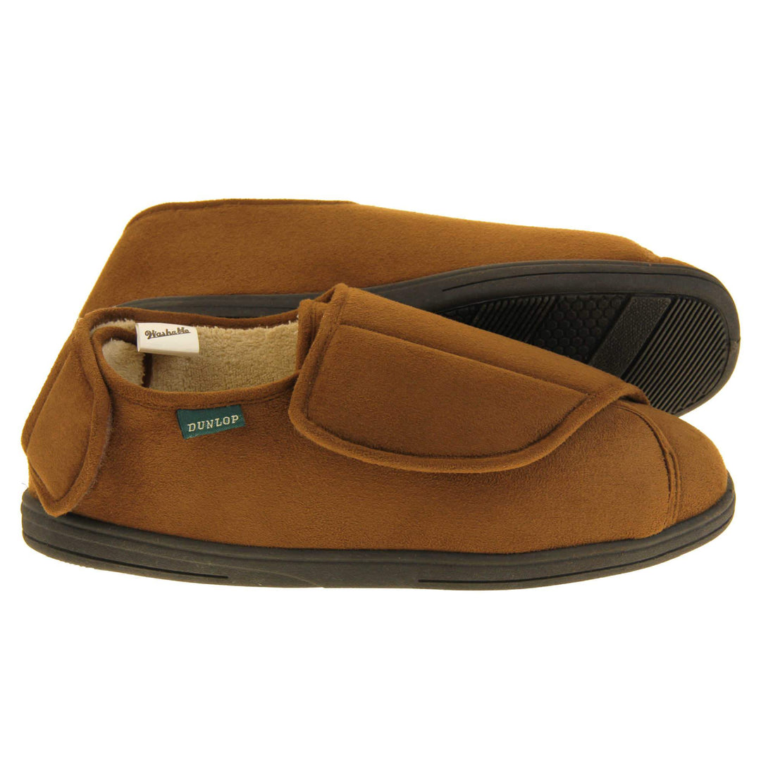 Mens adjustable slippers. Full back slippers with brown upper. Adjustable touch fasten strap to the top of the foot and around the back of the heel. Small white label on the outside rim, with Dunlop branding sewn in black. Cream faux fur lining. Firm black sole. Both feet from side profile with left foot on its side to show the sole.