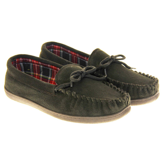 Mens plaid slippers. Moccasin style slipper with dark brown suede upper and leather bow to the top. Blue and red tartan plaid lining. Dark brown synthetic sole. Both feet together at an angle.