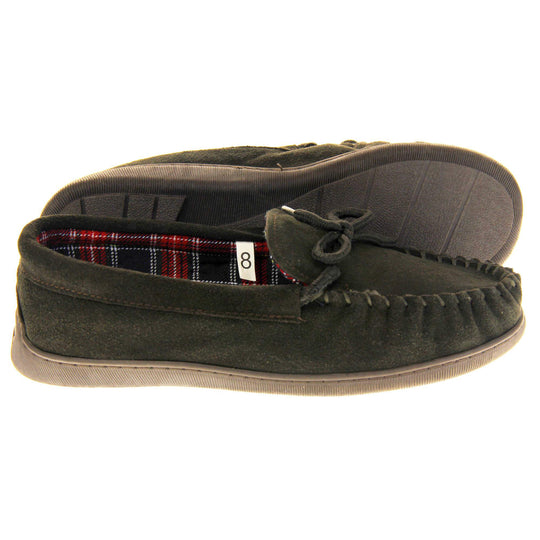 Mens plaid slippers. Moccasin style slipper with dark brown suede upper and leather bow to the top. Blue and red tartan plaid lining. Dark brown synthetic sole. Both feet from a side profile with the left foot on its side to show the sole.