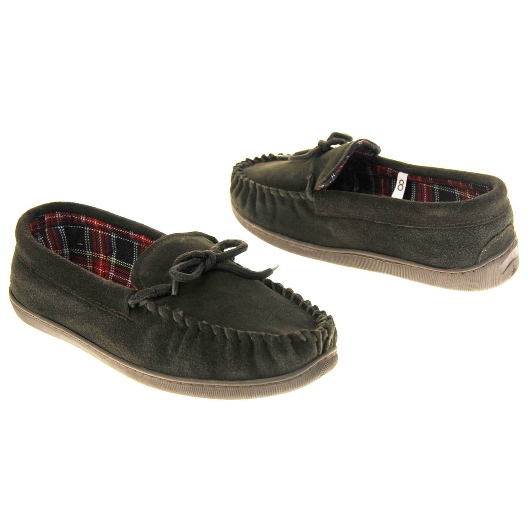 Mens plaid slippers. Moccasin style slipper with dark brown suede upper and leather bow to the top. Blue and red tartan plaid lining. Dark brown synthetic sole. Both shoes spaced apart, facing top to tail at an angle.