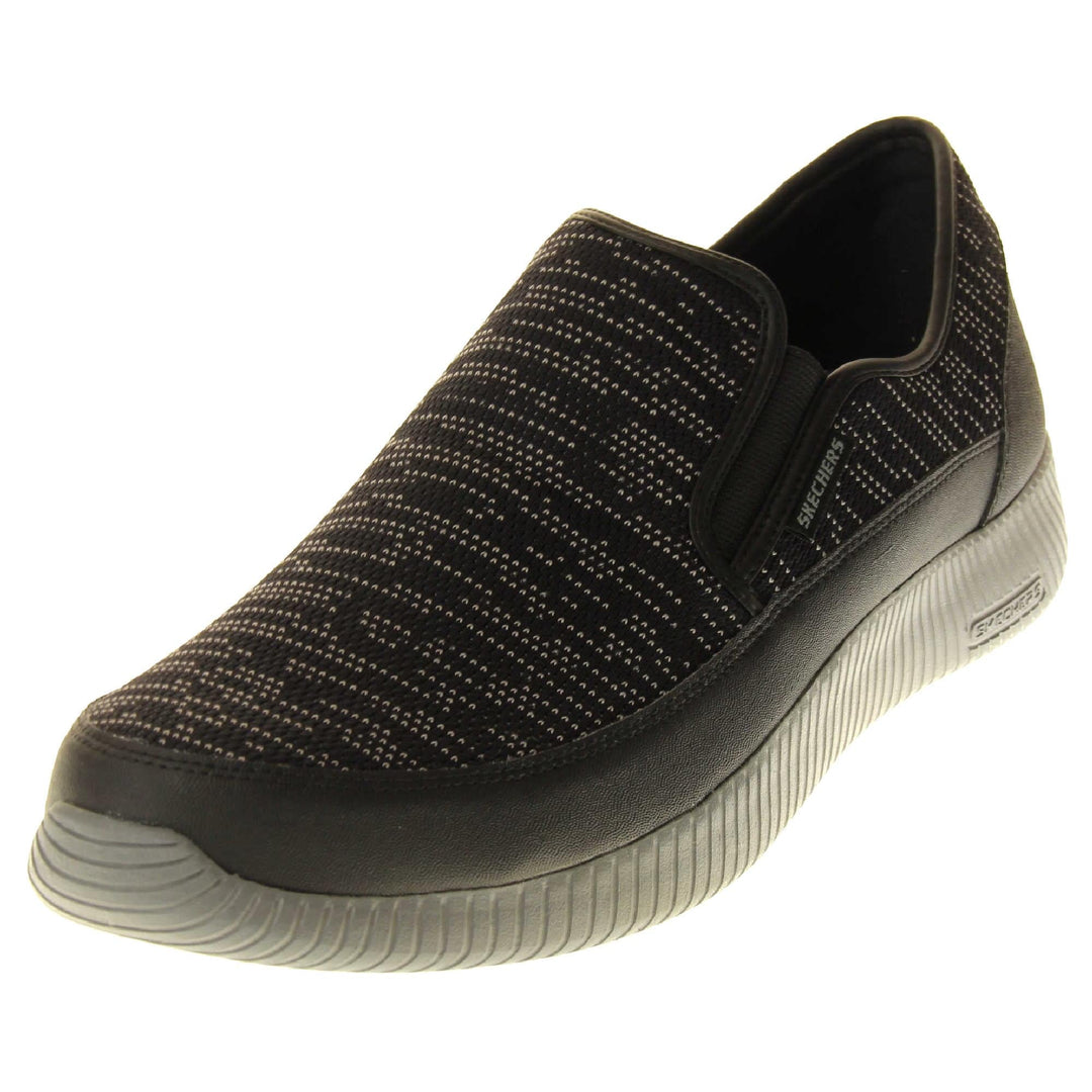 Mens slip on Skechers. Espadrille loafer style shoes with a trainer sole. Black textile upper with white stitch detail. Skechers S logo to the back. Grey thick sole with grip to the bottom. Black textile lining. Left foot at an angle.