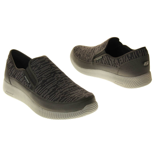 Mens slip on Skechers. Espadrille loafer style shoes with a trainer sole. Black textile upper with white stitch detail. Skechers S logo to the back. Grey thick sole with grip to the bottom. Black textile lining. Both feet from a slight angle facing top to tail.