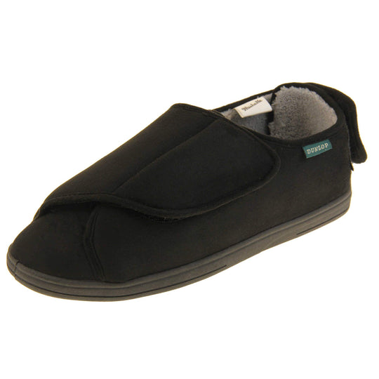 Mens adjustable slippers. Full back slippers with black upper. Adjustable touch fasten strap to the top of the foot and around the back of the heel. Small white label on the outside rim, with Dunlop branding sewn in black. Grey faux fur lining. Firm black sole. Left foot at an angle.