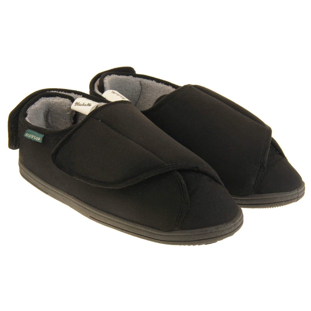 Mens adjustable slippers. Full back slippers with black upper. Adjustable touch fasten strap to the top of the foot and around the back of the heel. Small white label on the outside rim, with Dunlop branding sewn in black. Grey faux fur lining. Firm black sole. Both feet together at an angle.