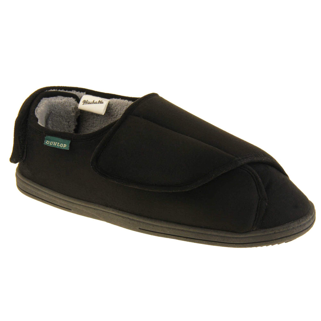 Mens adjustable slippers. Full back slippers with black upper. Adjustable touch fasten strap to the top of the foot and around the back of the heel. Small white label on the outside rim, with Dunlop branding sewn in black. Grey faux fur lining. Firm black sole. Right foot at an angle.