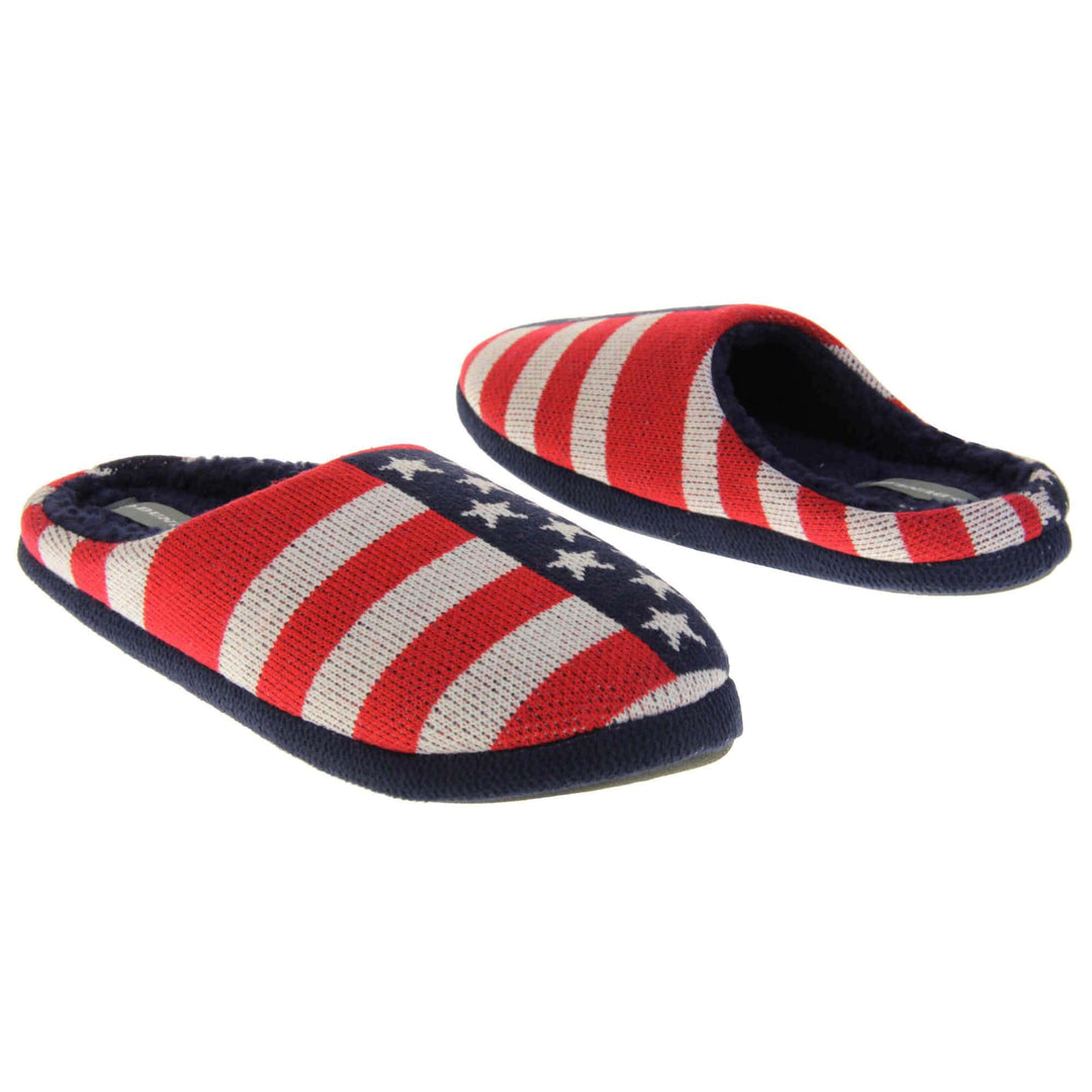 Mens American Flag slippers. Mens slippers in a mule style. With red, white and blue USA flag knit fabric upper. Blue faux fur lining. Black hard synthetic soles with grip to the base. Both feet from an angle facing top to tail.