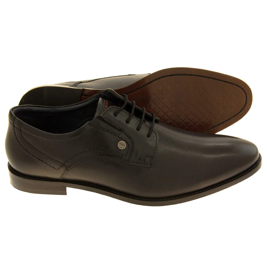 Mens black dress shoes. Mens formal shoes with a black leather upper and black stitching detail. Black laces to the front. Small silver stud on the side with S.Oliver written on. Black sole with very slight heel. Black lining. Both feet from a side profile with left foot on its side behind the right to show its sole.