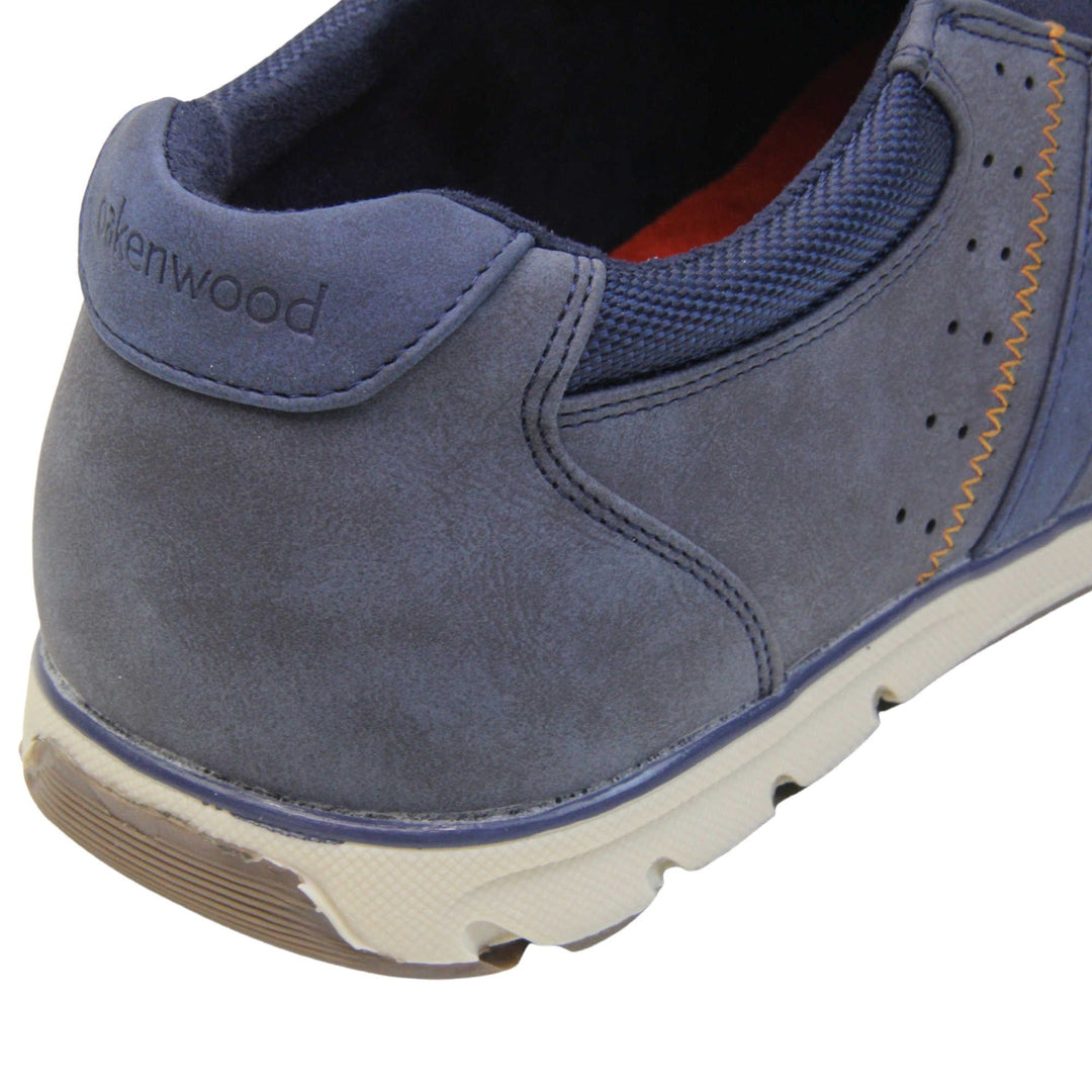 Mens blue suede trainers. Slip on trainers with navy blue faux suede uppers. Elasticated side gussets in dark blue and a navy diagonal stripe to the side of the shoe. Dark blue collar around the neck of the shoe with Oakenwood branding to the heel. Dark blue lining and a white outsole with grey sole. Left foot close up of the heel of the shoe to show the lining and heel branding of the shoe.