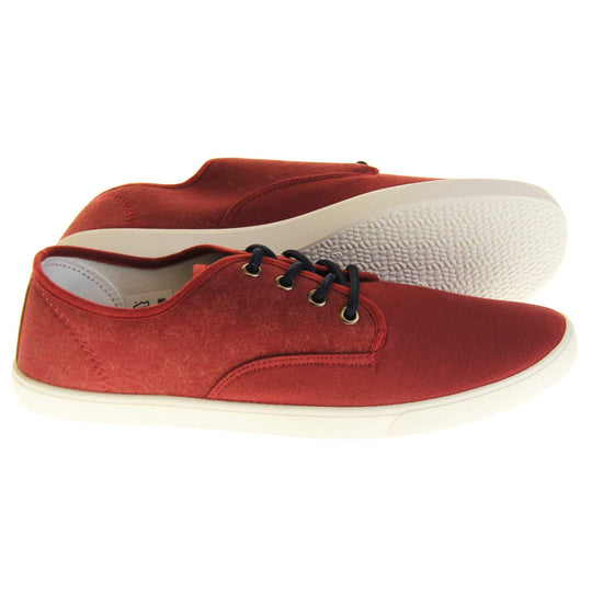 Mens canvas pumps. Burgundy red canvas upper with black laces. White synthetic sole and white textile lining. Both feet from a side profile with left foot behind the right on its side to show the sole