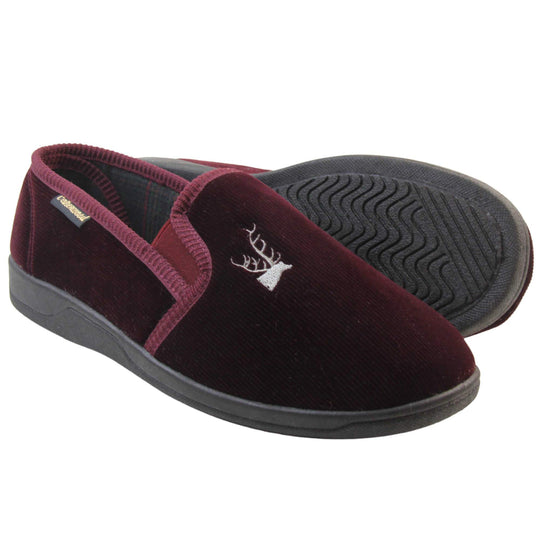 Classic Slippers. Mens full back slippers with a burgundy red velour uppers. Red elasticated panels joining the tongue to the top of the slippers. Grey stag head detail embroidered onto the top of the upper, near the tongue. Small black label on the outside rim, with Oakenwood branding sewn in gold. Plaid textile lining.  Both feet from side profile with left foot on its side to show the sole.
