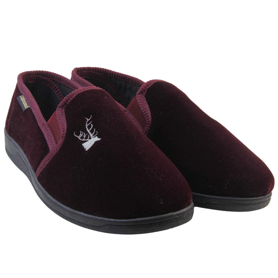 Classic Slippers. Mens full back slippers with a burgundy red velour uppers. Red elasticated panels joining the tongue to the top of the slippers. Grey stag head detail embroidered onto the top of the upper, near the tongue. Small black label on the outside rim, with Oakenwood branding sewn in gold. Plaid textile lining. Both feet together at an angle.