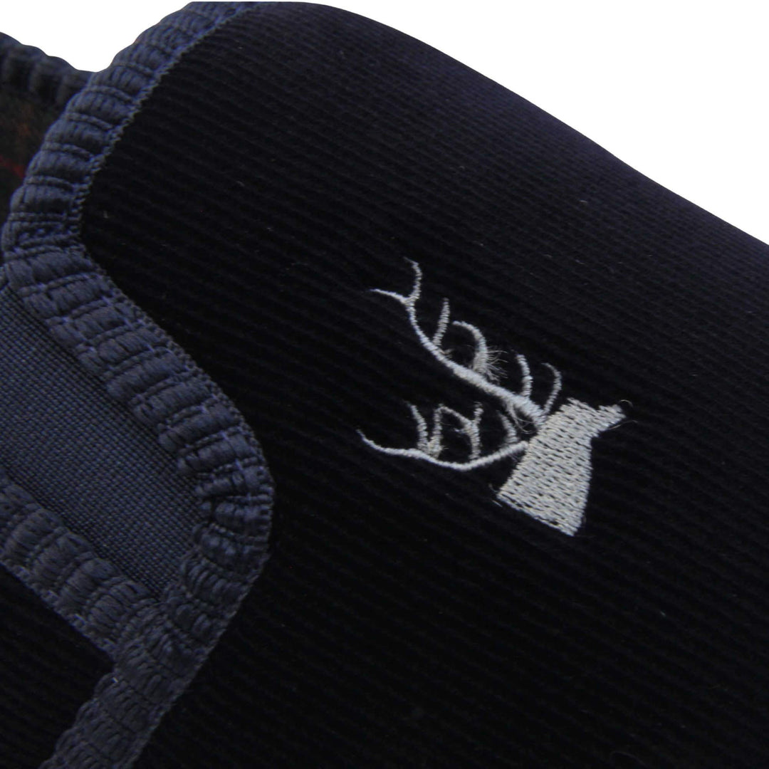 Mens Comfortable Slippers. Full back slippers for men with a navy blue velour uppers. Navy elasticated panels joining the tongue to the top of the slippers. Grey stag head detail embroidered onto the top of the upper, near the tongue. Small navy label on the outside rim, with Oakenwood branding sewn in gold. Navy textile lining. Close up of the top of the slipper to show the stag detailing.
