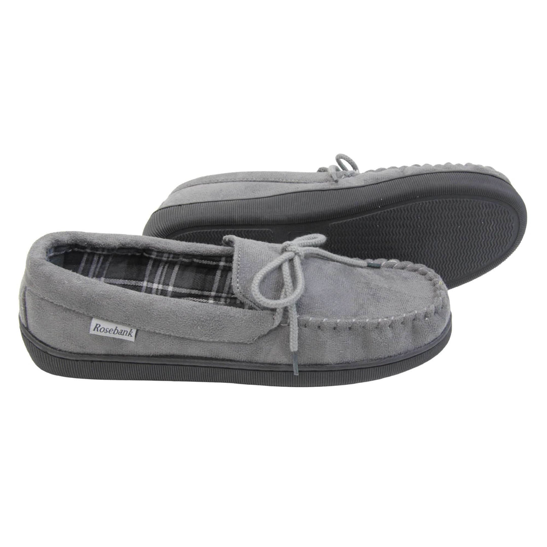 Mens grey moccasin slippers. Moccasin style slipper with grey faux suede upper and rope style bow to the top. Grey Rosebank label to the outside. Dark and light grey and white plaid textile lining. Black rubber sole. Both feet from a side profile with the left foot on its side to show the sole.