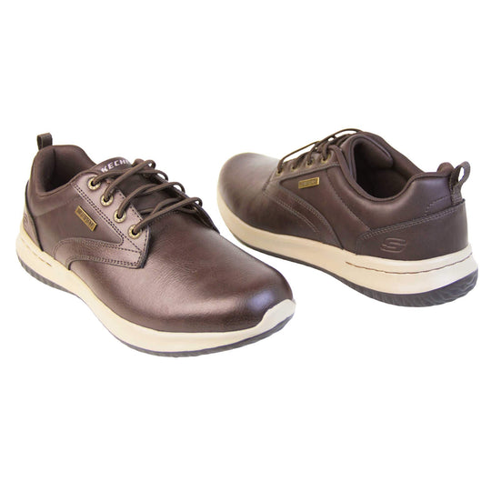 Mens leather skechers. Brown leather upper in trainer style shoe with brown stitching detail. Brown laces with gold eyelets for laces. White Skechers branding on tongue. Small gold rectangle tag to the side saying waterproof. Small S logo to the side of the heel. White outsole with black base. Brown textile lining. Both shoes at a slight angle facing top to tail.