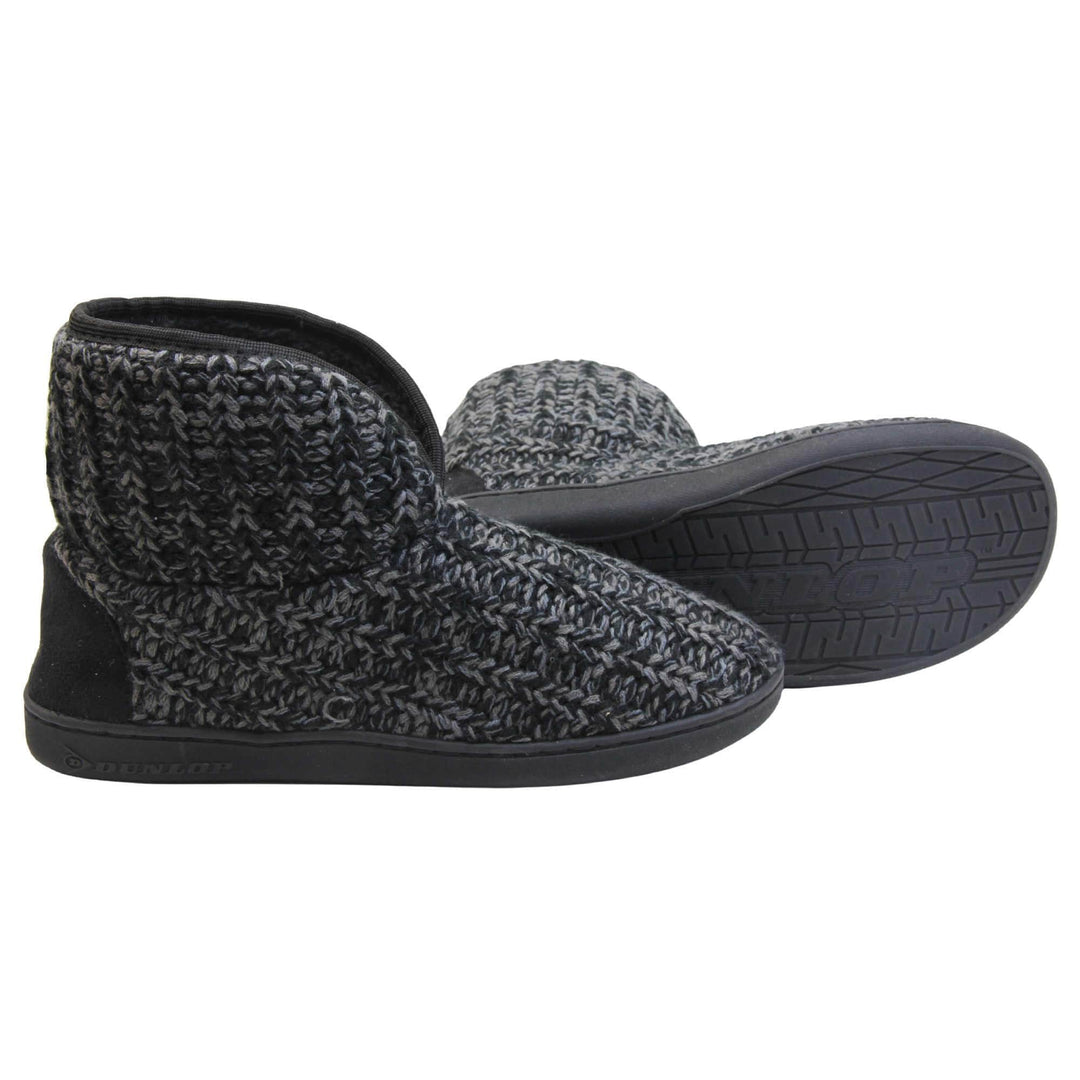 Mens memory foam slipper boots. Slipper boots with a black knit upper. Black fabric piping around the collar. Black textile patch over the heel to reinforce. Thick black synthetic sole with Dunlop branding on. Black faux fur lining. Both slippers from side profile with left foot on its side behind the right to show the sole.