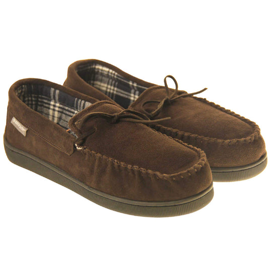 Mens moccasin slippers. Moccasin style slipper with brown suede upper and leather bow to the top. Grey Dunlop label to the outside. Grey and white plaid textile lining. Black rubber sole.  Both feet together at an angle.