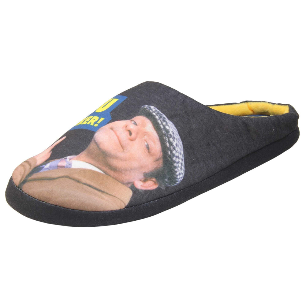 Mens mule novelty slippers. Mens slippers in a mule style. With black fabric upper with Del Boy from Only Fools and Horses printed on it and pointing. The words you plonker! in bold yellow font outlined in blue above his pointing finger. Blue fabric insole with yellow Totters independent trading logo on. Yellow fleece lining. Black hard synthetic soles with bumpy grip to the base. Left foot at an angle.
