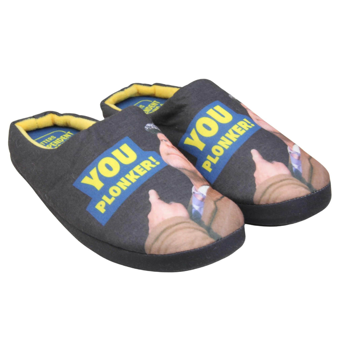 Mens mule novelty slippers. Mens slippers in a mule style. With black fabric upper with Del Boy from Only Fools and Horses printed on it and pointing. The words you plonker! in bold yellow font outlined in blue above his pointing finger. Blue fabric insole with yellow Totters independent trading logo on. Yellow fleece lining. Black hard synthetic soles with bumpy grip to the base. Both feet together from a  slight angle.