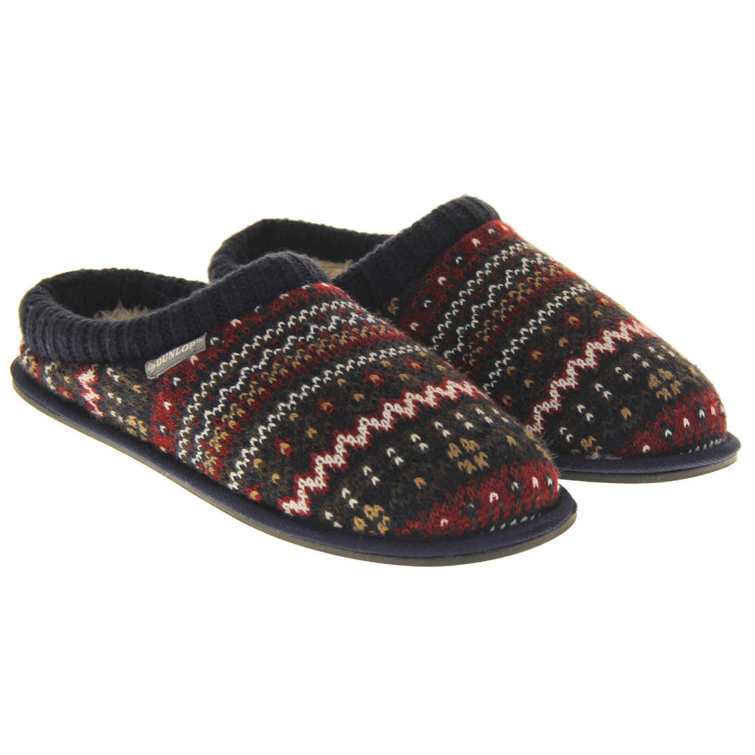 Mens navy mule slippers. Mens slippers in a mule style. With navy blue knit fabric upper with brown, red and white pattern. Cream faux fur lining. Black hard synthetic soles with grip to the base. Both feet together from a slight angle.