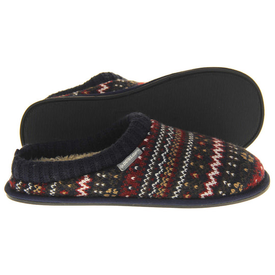 Mens navy mule slippers. Mens slippers in a mule style. With navy blue knit fabric upper with brown, red and white pattern. Cream faux fur lining. Black hard synthetic soles with grip to the base. Both feet from a side profile with the left foot on its side to show the sole.