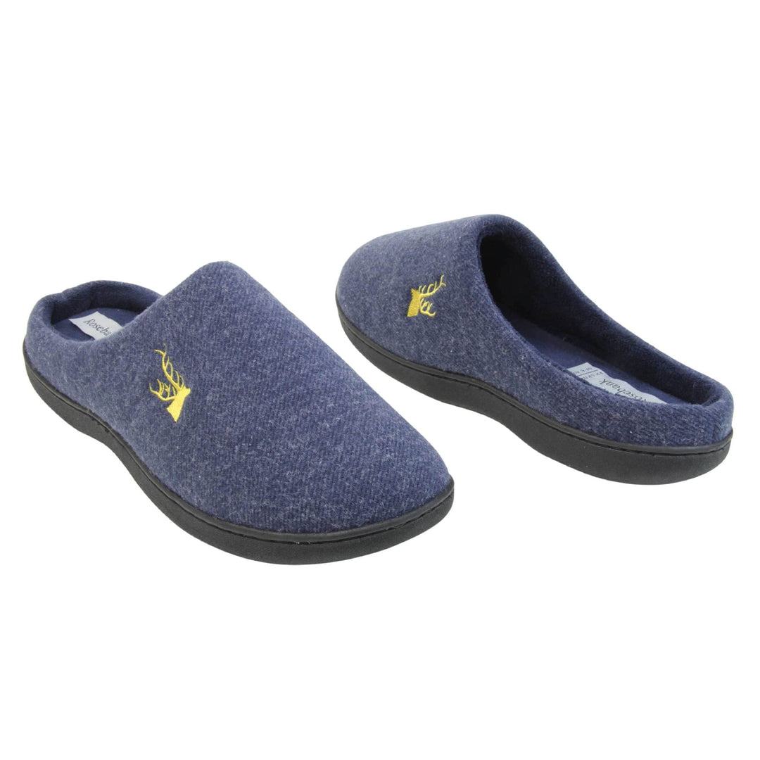 Mens slip on slippers. Mule style slippers with blue fleece uppers with an embroidered stag head to the top, on the outside. Blue terry lining and firm black sole. Both feet at an angle facing top to tail.
