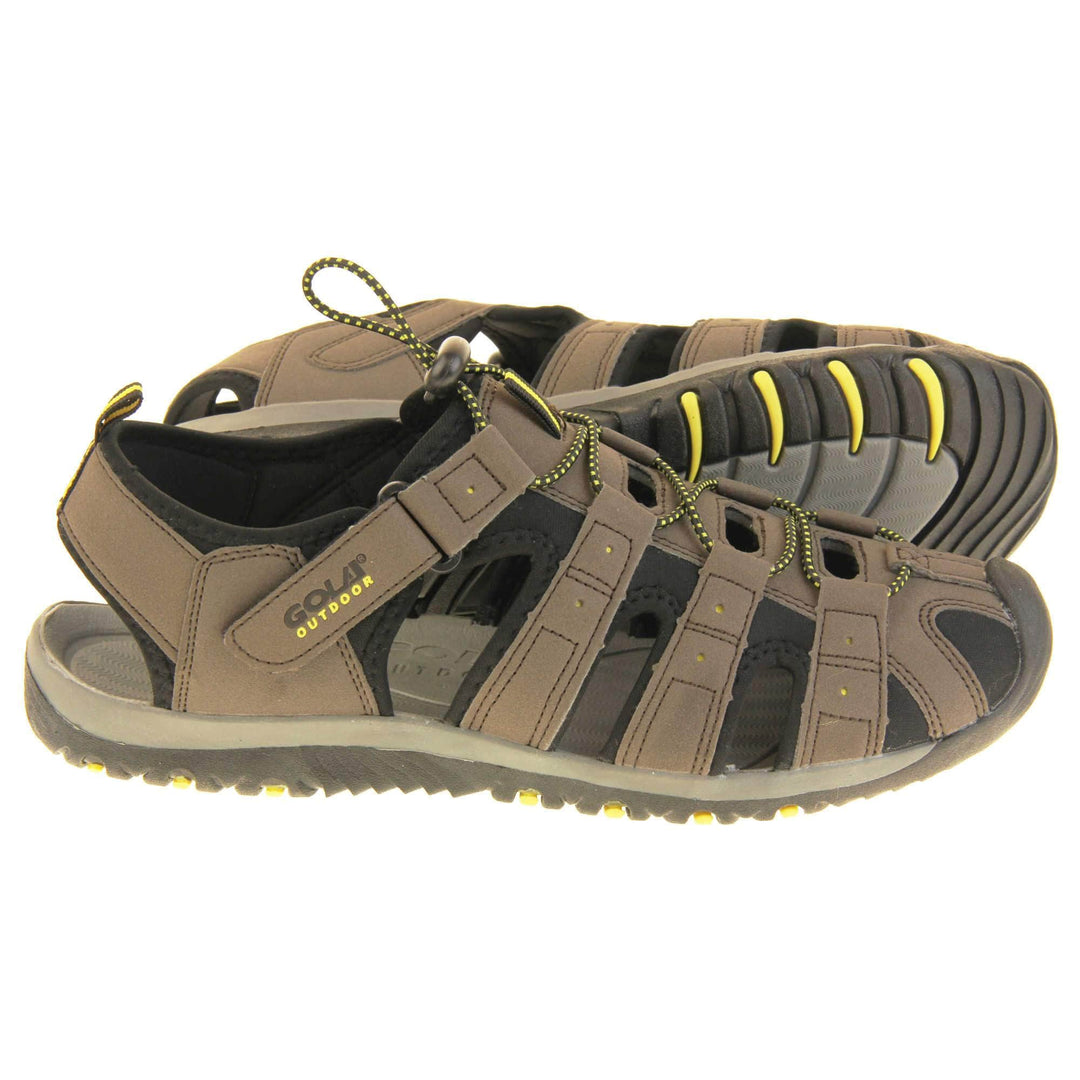 Mens sport sandals. Traditional style sandal with brown and black fabric strappy upper. Black rubber toe caps and black synthetic sole with yellow grips to the bottom. Elasticated laces to the front of the shoe and touch fasten strap by the ankle. Both feet from side profile with the left foot on its side behind the right to show its sole.
