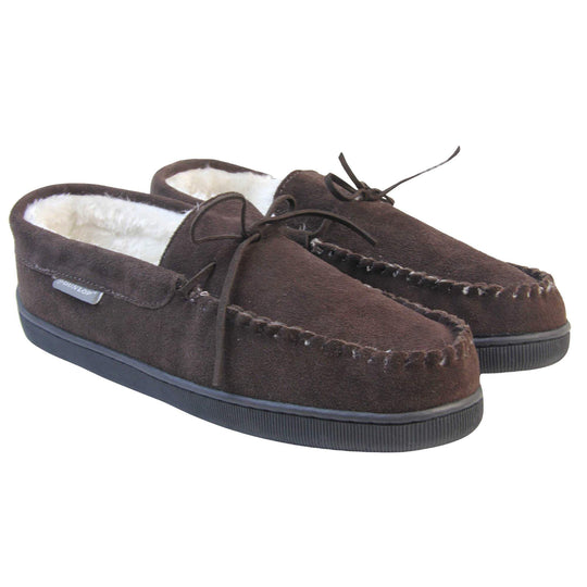 Mens suede moccasin slippers. Closed back slippers in a moccasin style with dark brown suede leather upper and bow. Cream faux fur lining. Thick black sole. Both feet together at an angle.