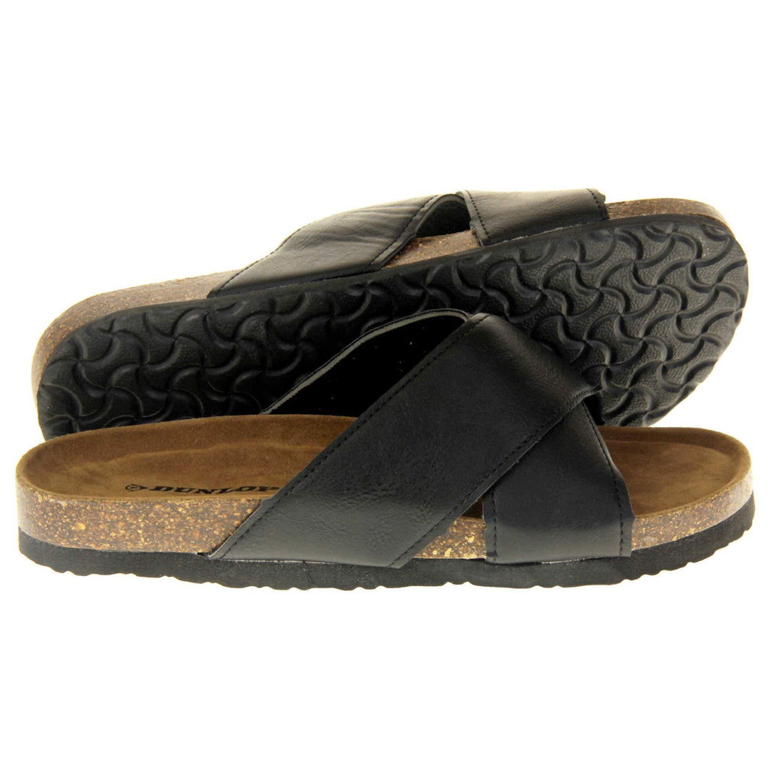 Mens two strap sandals. Black faux leather upper of two thick straps crossed over each other. Brown faux suede insole with Dunlop branding. Cork style outsole with black base. Both feet from a side profile with left foot behind the right on its side to show the sole.
