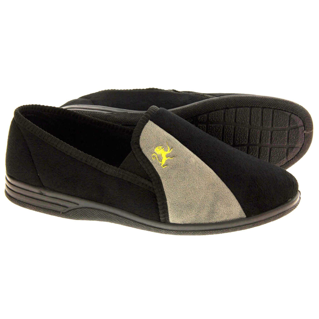 Mens Velour Slippers. Full back slippers for men with a black velour uppers with grey stripe with a yellow embroidered lion on. Black elasticated panels joining the tongue to the top of the slippers. Black textile lining. Both feet from side profile with left foot on its side to show the sole.