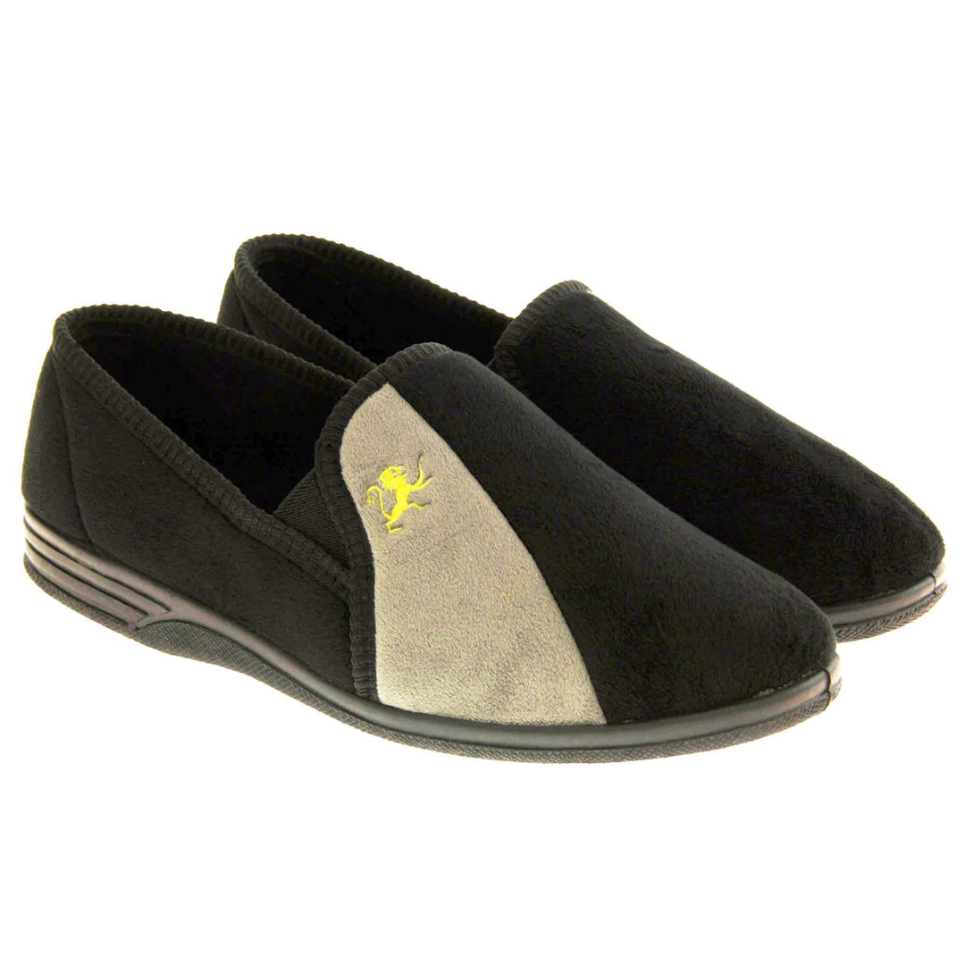 Mens Velour Slippers. Full back slippers for men with a black velour uppers with grey stripe with a yellow embroidered lion on. Black elasticated panels joining the tongue to the top of the slippers. Black textile lining. Both feet together at an angle.