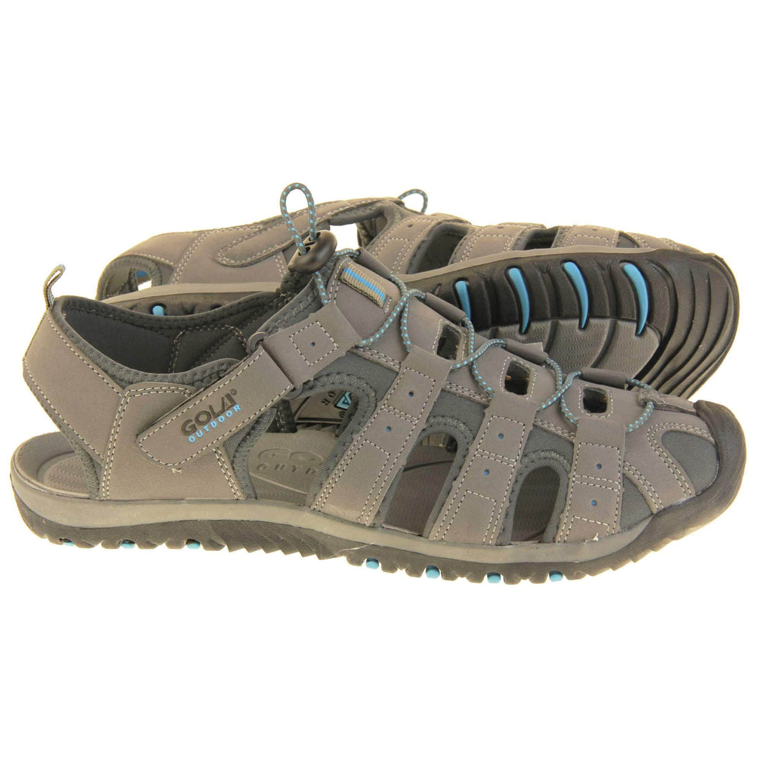 Mens walking sandals. Traditional style sandal with Light grey and dark grey fabric strappy upper. Black rubber toe caps and black synthetic sole with blue grips to the bottom. Elasticated laces to the front of the shoe and touch fasten strap by the ankle.  Both feet from side profile with the left foot on its side behind the right to show its sole.