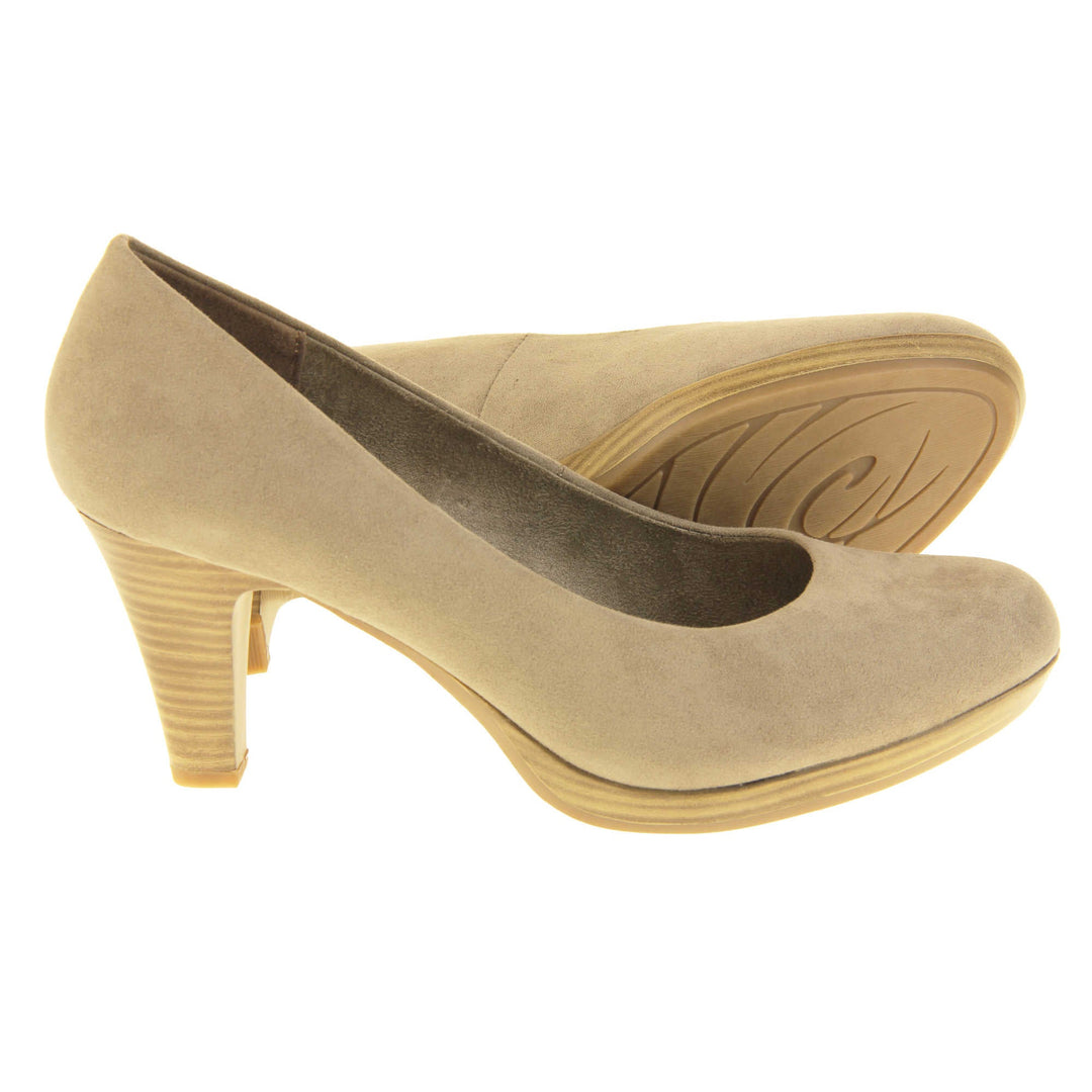 Mid heel court shoes. Womens shoes with a taupe faux suede upper. Pale gold metallic insole with Marco Tozzi branding. Taupe faux suede lining. Wood appearance mid block heel and small platform. Both feet from a side profile with the left foot on its side behind the the right foot to show the sole.