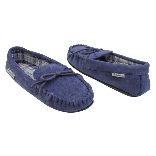 Moccasin slippers womens. Moccasin style slipper with navy blue faux suede upper and rope style bow to the top. Grey Rosebank label to the outside. Blue and white plaid textile lining. Black rubber sole. Both shoes spaced apart, facing top to tail at an angle.