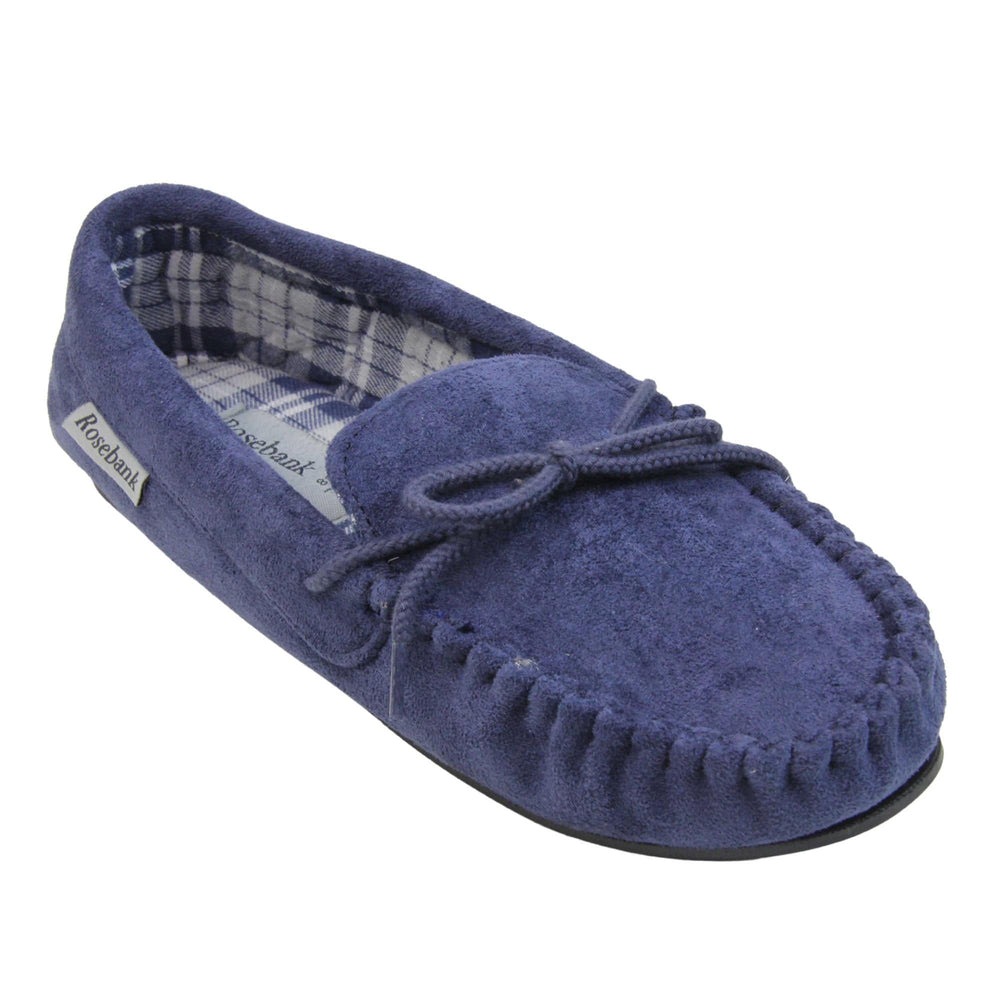 Moccasin slippers womens. Moccasin style slipper with navy blue faux suede upper and rope style bow to the top. Grey Rosebank label to the outside. Blue and white plaid textile lining. Black rubber sole. Right foot at an angle.