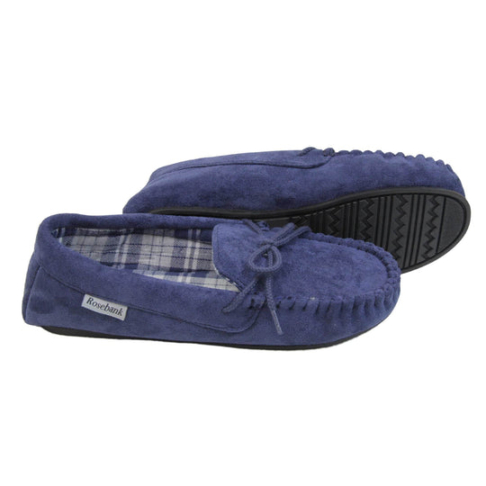 Moccasin slippers womens. Moccasin style slipper with navy blue faux suede upper and rope style bow to the top. Grey Rosebank label to the outside. Blue and white plaid textile lining. Black rubber sole. Both feet from a side profile with the left foot on its side to show the sole.