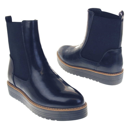 Navy flat ankle boots. Faux leather, tall Chelsea boot style with a navy blue coloured upper. Blue elasticated panels at the ankles and a navy loop at the heel to help pull them on. Black coloured low platform sole. Both feet from a slight angle facing top to tail.