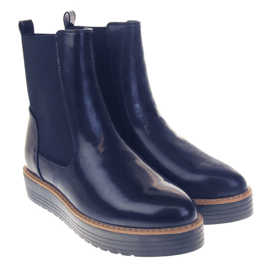 Navy flat ankle boots. Faux leather, tall Chelsea boot style with a navy blue coloured upper. Blue elasticated panels at the ankles and a navy loop at the heel to help pull them on. Black coloured low platform sole. Both feet together from an angle.