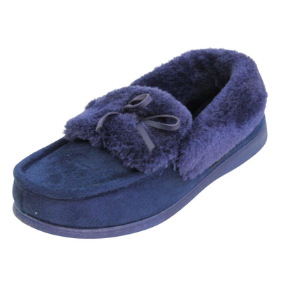 Navy moccasin slippers. Moccasin style slipper with a navy blue faux suede upper and bow to the top. Navy faux fur collar, tongue and lining. Navy rubber sole. Left foot at an angle.