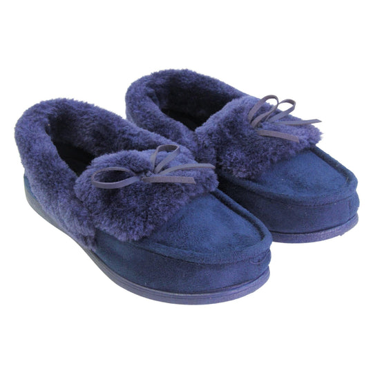 Navy moccasin slippers. Moccasin style slipper with a navy blue faux suede upper and bow to the top. Navy faux fur collar, tongue and lining. Navy rubber sole. Both feet together at an angle.