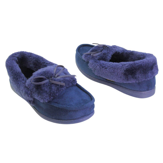 Navy moccasin slippers. Moccasin style slipper with a navy blue faux suede upper and bow to the top. Navy faux fur collar, tongue and lining. Navy rubber sole. Both feet at an angle facing top to tail.
