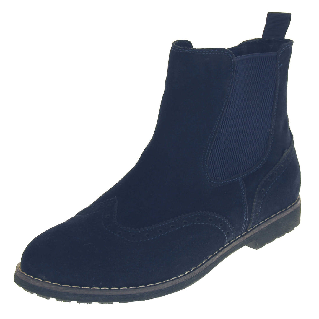 Navy suede brogue boots. Ankle boot style with brogue detailing. With a navy blue suede upper. Navy elasticated panels at the ankles and a blue loop at the heel to help pull them on. Black coloured sole with a very slight heel. Left foot at an angle.